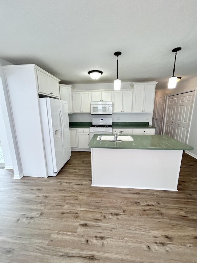 kitchen with wood finished floors, white appliances, dark countertops, and a sink