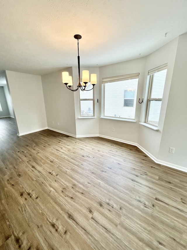 unfurnished dining area with baseboards, a chandelier, and wood finished floors