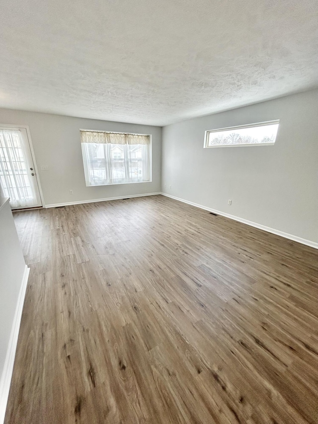 unfurnished living room featuring a textured ceiling, wood finished floors, and baseboards