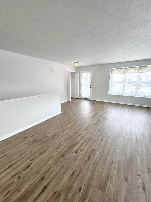 unfurnished living room featuring a textured ceiling, baseboards, and wood finished floors