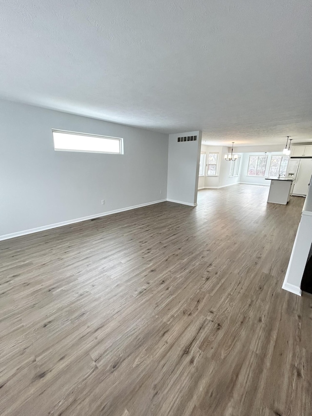 unfurnished living room featuring a chandelier, a textured ceiling, wood finished floors, visible vents, and baseboards