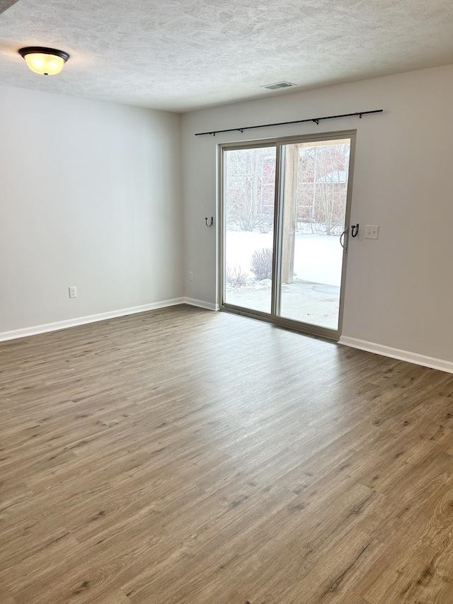 spare room featuring a textured ceiling, wood finished floors, visible vents, and baseboards