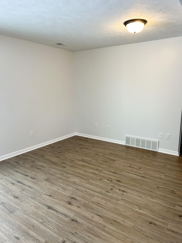 spare room featuring dark wood-style floors, a textured ceiling, visible vents, and baseboards