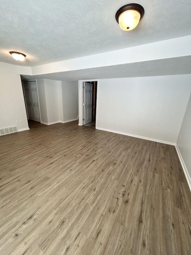 spare room with visible vents, a textured ceiling, baseboards, and wood finished floors