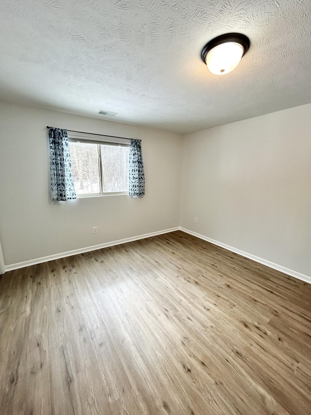 empty room featuring wood finished floors, visible vents, and baseboards