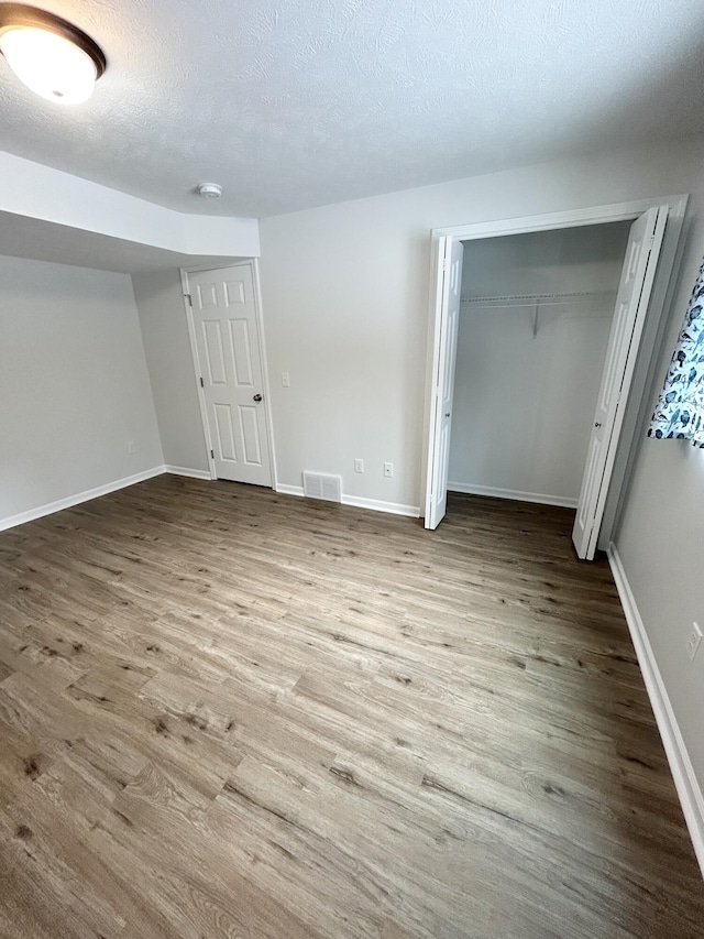 interior space featuring baseboards, a textured ceiling, visible vents, and wood finished floors