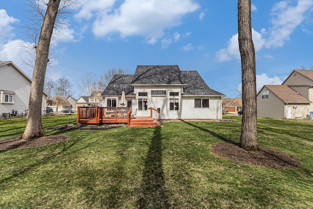 back of house with roof with shingles, a lawn, and a wooden deck