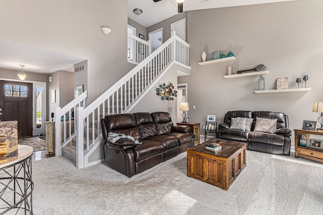 living area with a towering ceiling, visible vents, stairway, and carpet flooring