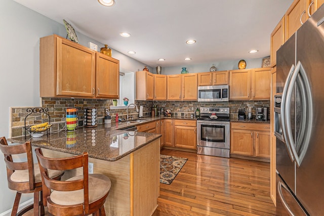 kitchen featuring decorative backsplash, hardwood / wood-style flooring, dark stone countertops, a peninsula, and stainless steel appliances