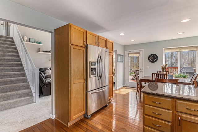 kitchen with recessed lighting, stainless steel refrigerator with ice dispenser, brown cabinets, dark stone counters, and hardwood / wood-style floors