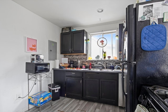 kitchen with light wood finished floors, decorative backsplash, a sink, dark cabinetry, and black appliances