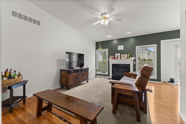 living room with light wood-style flooring, a fireplace with flush hearth, visible vents, and a ceiling fan