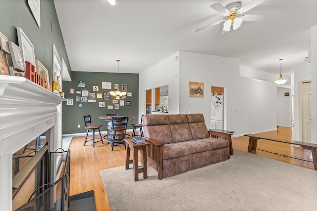 living room featuring light wood-type flooring, a fireplace, baseboards, and ceiling fan with notable chandelier