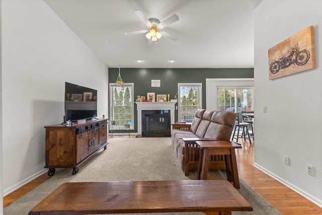 living area featuring a fireplace with flush hearth, light wood-type flooring, baseboards, and a ceiling fan