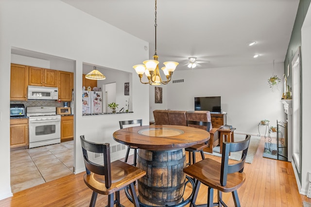 dining area featuring baseboards, visible vents, light wood finished floors, and ceiling fan with notable chandelier