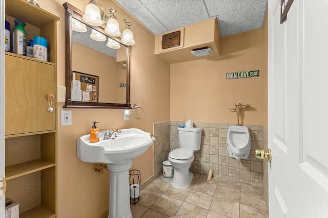 half bathroom with toilet, a wainscoted wall, visible vents, tile walls, and tile patterned floors