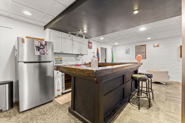 kitchen with brick wall, a paneled ceiling, freestanding refrigerator, and white cabinets