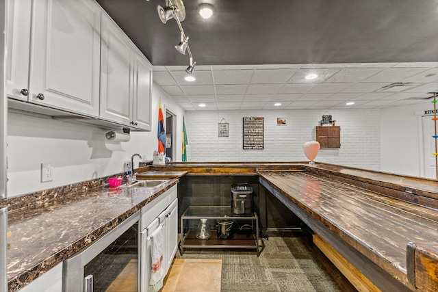 kitchen with a drop ceiling, wine cooler, white cabinetry, a sink, and recessed lighting