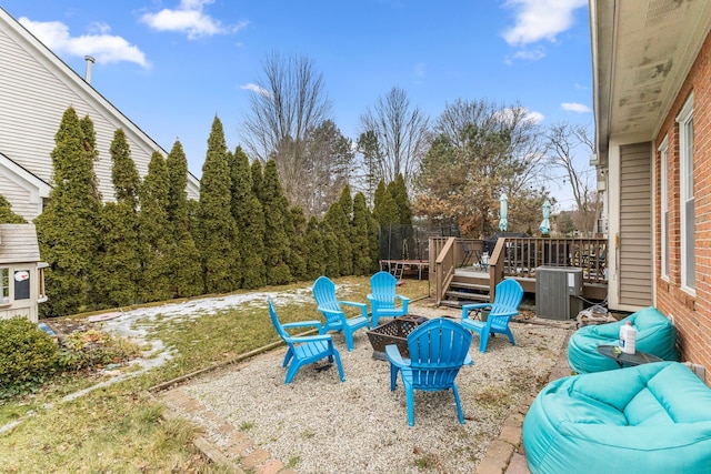 view of yard featuring a fire pit, a trampoline, central AC unit, and a wooden deck