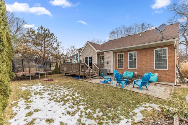 back of house featuring a trampoline, brick siding, a yard, a patio area, and a wooden deck