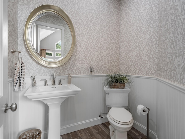 bathroom with wood finished floors, wainscoting, and wallpapered walls