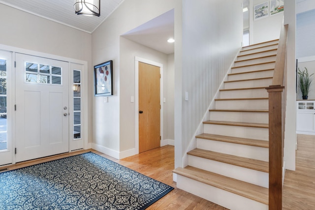 foyer with light wood-style floors, vaulted ceiling, baseboards, and stairs