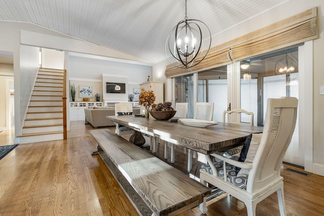 dining room with vaulted ceiling, wood finished floors, stairs, and an inviting chandelier