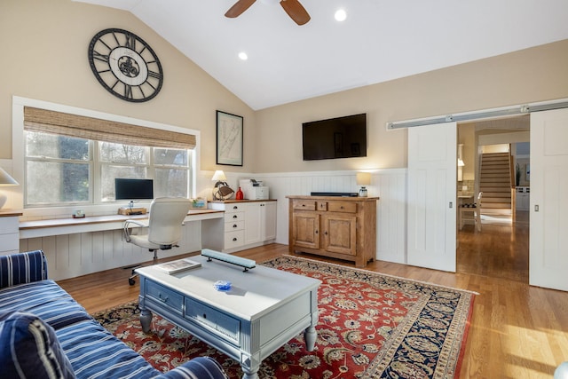 living room featuring a barn door, a wainscoted wall, vaulted ceiling, light wood-type flooring, and built in desk