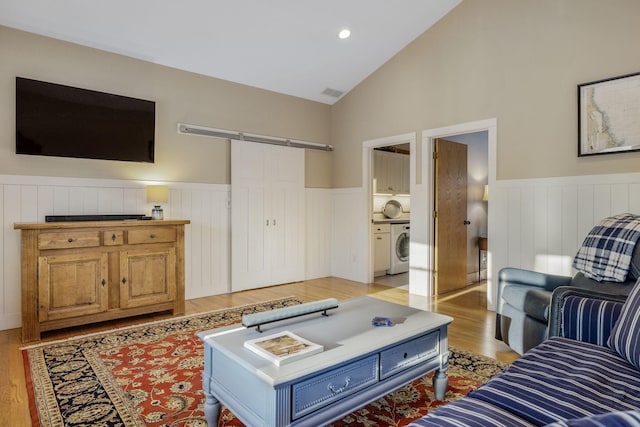 living area featuring lofted ceiling, a barn door, washer / clothes dryer, and a wainscoted wall