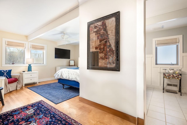 bedroom featuring a ceiling fan, a wainscoted wall, beamed ceiling, and wood finished floors