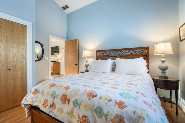 bedroom featuring high vaulted ceiling, visible vents, a closet, and wood finished floors