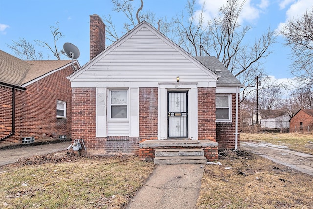 bungalow featuring a shingled roof, brick siding, and a chimney