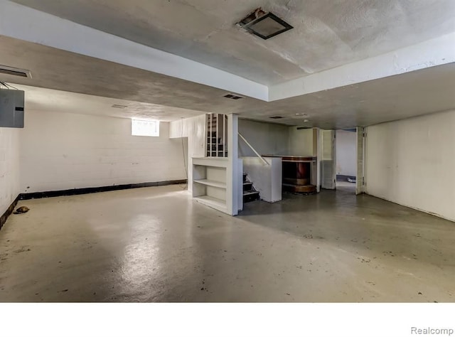 basement featuring stairway, concrete block wall, visible vents, and electric panel