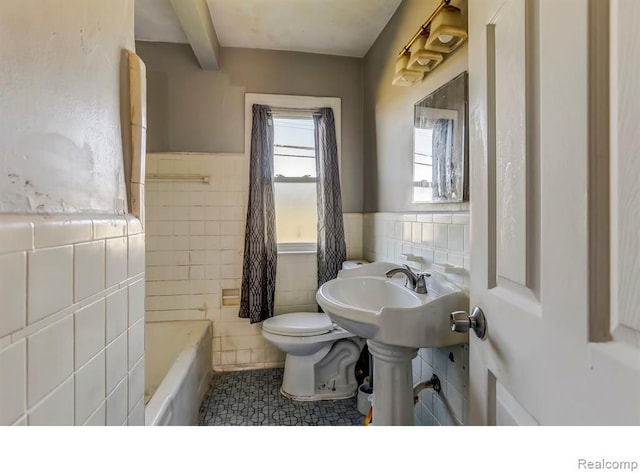 full bath featuring toilet, a wainscoted wall, a sink, tile walls, and a bathtub