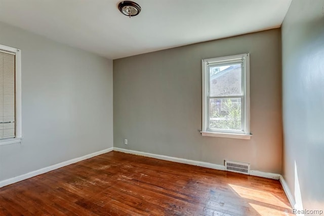 empty room featuring wood-type flooring, visible vents, and baseboards