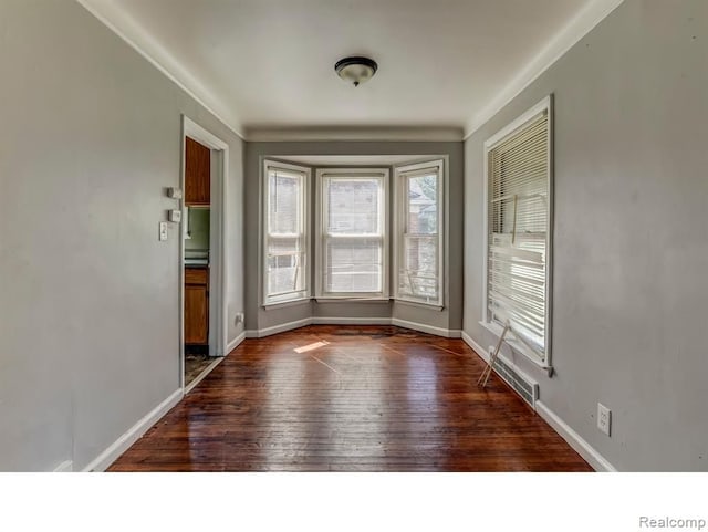 unfurnished room featuring dark wood-type flooring, ornamental molding, and baseboards