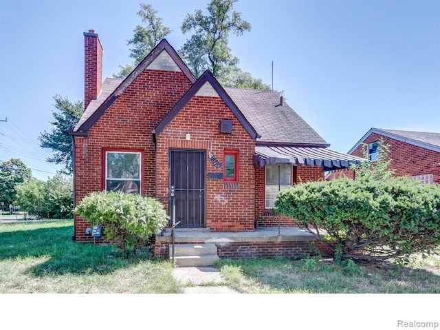 view of front of home featuring a front yard, brick siding, and a chimney