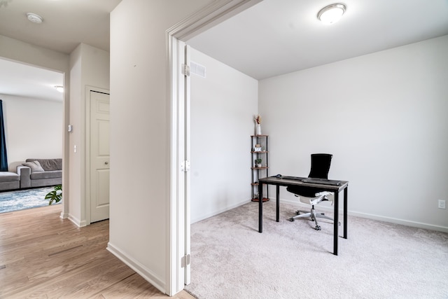 office featuring light wood-style flooring, baseboards, and light colored carpet