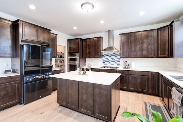 kitchen featuring stainless steel appliances, dark brown cabinets, light countertops, wall chimney exhaust hood, and light wood finished floors