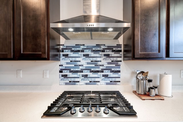 kitchen with stainless steel gas cooktop, light countertops, dark brown cabinets, and wall chimney exhaust hood