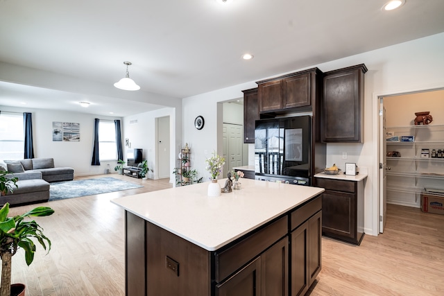 kitchen featuring refrigerator, light wood finished floors, light countertops, open floor plan, and dark brown cabinets