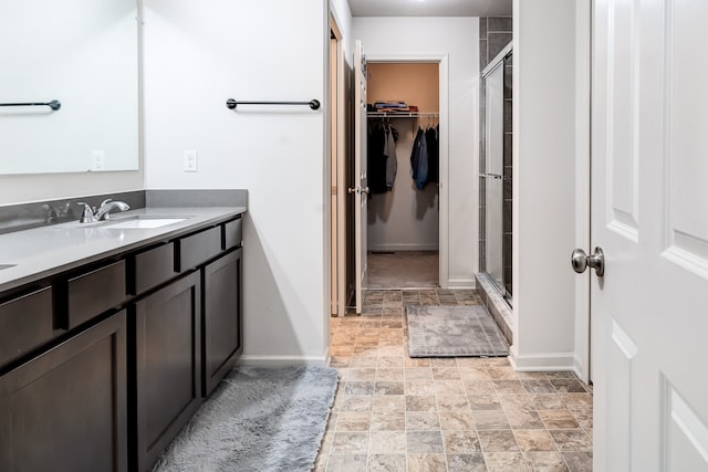 bathroom with a stall shower, a walk in closet, stone finish flooring, and vanity