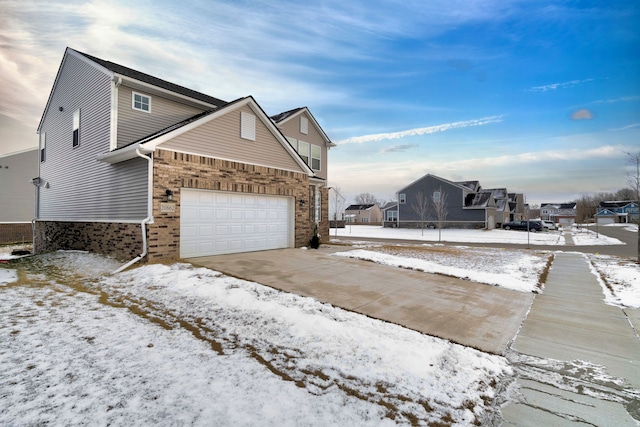 snow covered property featuring a garage, a residential view, concrete driveway, and brick siding