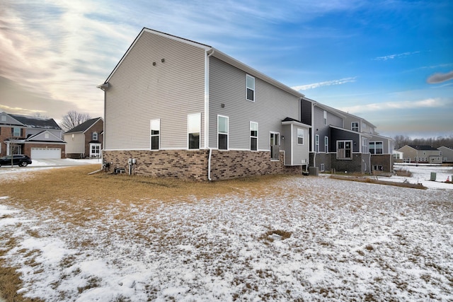 snow covered property with central air condition unit, a residential view, and brick siding