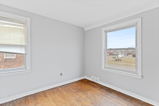 spare room with wood-type flooring, visible vents, and baseboards