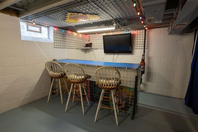 bar featuring concrete flooring, concrete block wall, under cabinet range hood, and a bar