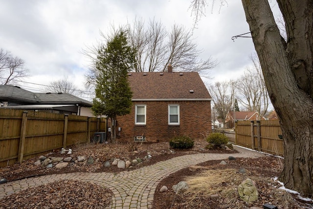 rear view of house featuring brick siding, a fenced backyard, and roof with shingles