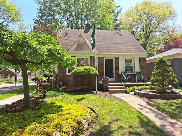 view of front of property featuring a chimney, a front lawn, a porch, and brick siding