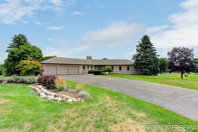 ranch-style home featuring a chimney, an attached garage, a front yard, and aphalt driveway