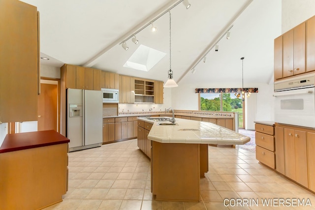 kitchen with white appliances, light countertops, hanging light fixtures, lofted ceiling with skylight, and an island with sink